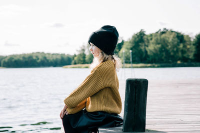 Side view of woman standing by lake against sky