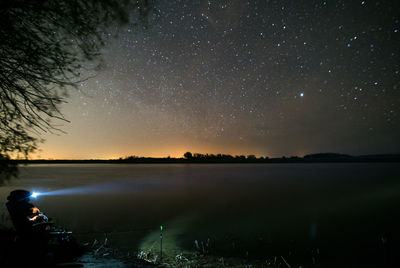 Man flashing light on lake against sky at night