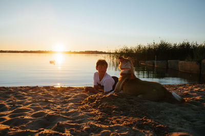 Young man sitting on beach against sky during sunset