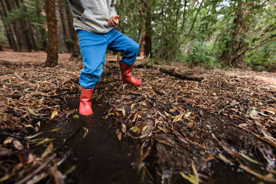 Young child with red boots stomping in mud in forest