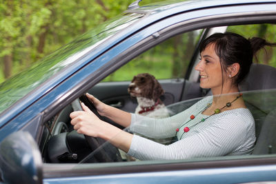 Woman with dog driving car seen through window