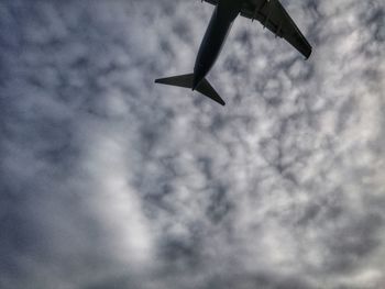 Low angle view of airplane flying against cloudy sky