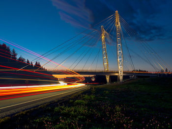 Light trails on bridge in city against blue sky