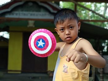 Portrait of cute boy with small shield standing at yard