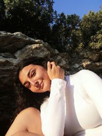 Young woman sitting on rock against trees