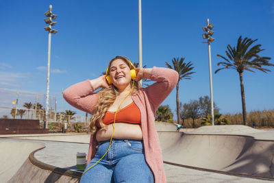 Young woman listening music sitting against sky