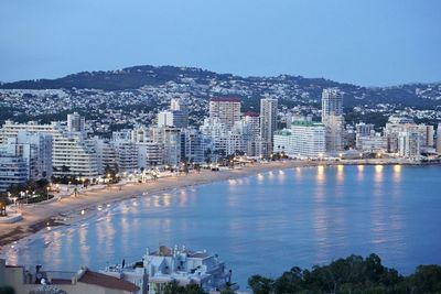 High angle view of illuminated buildings by sea against sky