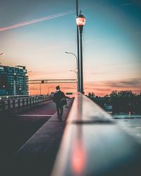 Silhouette man walking on illuminated bridge against sky at sunset