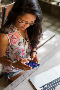 High angle view of woman using phone while sitting on table