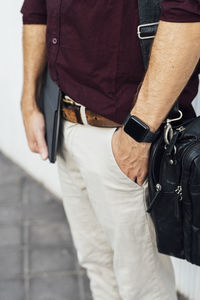 Businessman with digital tablet and shoulder bag standing with hands in pockets on footpath