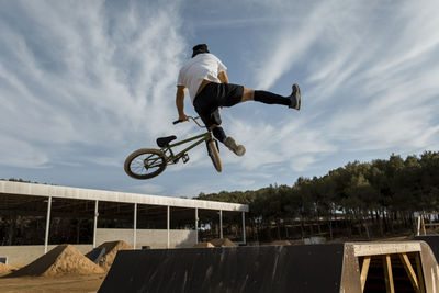 Man doing stunt over ramp at bike park against sky