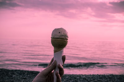 Hand holding ice cream against sea during sunset
