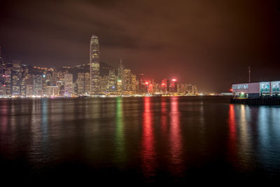 Illuminated city by river against sky at night