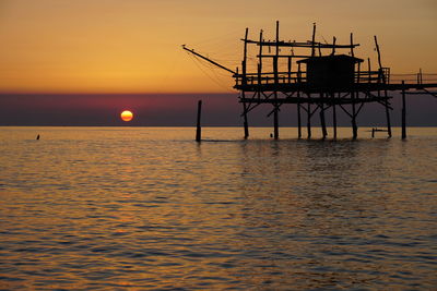 Silhouette built structure over sea against sky during sunset