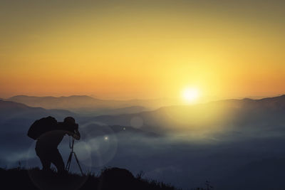 Silhouette man photographing against sky during sunset