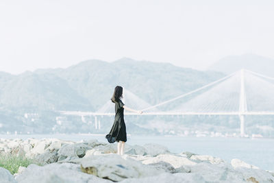 Woman standing on rock against clear sky