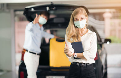 The taxi driver in medical mask putting yellow suitcases of women in the trunk of a car.