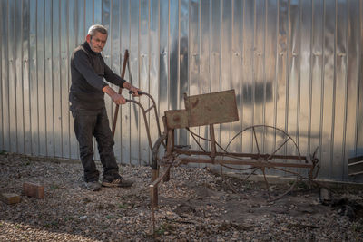 Portrait of senior man holding equipment while standing on field against wall