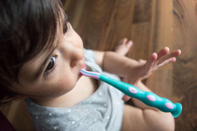 High angle view of cute girl with toothbrush in mouth sitting on floor