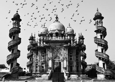 Flock of birds flying over mahabat maqbara against sky