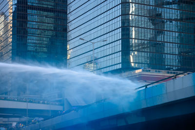 Low angle view of smoke emitting from glass building in city