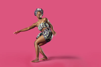 Portrait of young woman dancing against pink background