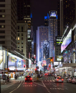 Cars on road amidst illuminated buildings at night