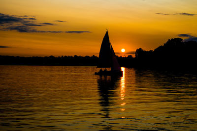 Silhouette boat sailing in lake against sky during sunset