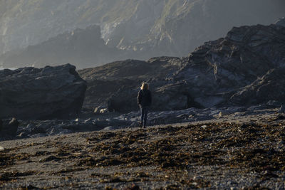 Rear view of woman walking at beach against rocky mountains