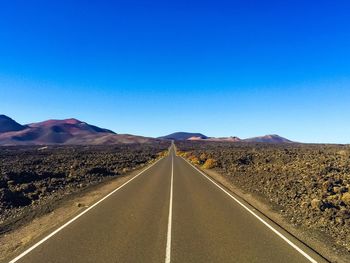 Empty road along landscape against clear blue sky