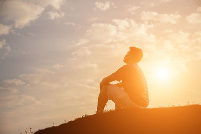 Side view of silhouette man sitting against sky during sunset