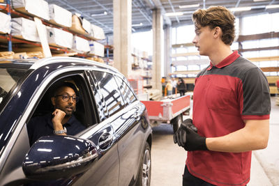 Mature man sitting in car talking with sales staff at hardware store