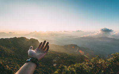 Copped hand of person against sky during sunset