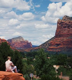 Rear view of man sitting on cliff against sky