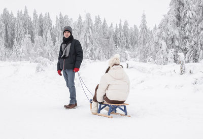 A young handsome guy is standing resting after sledding his girlfriend in a snowy winter forest