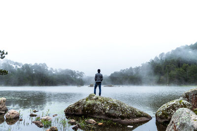 Rear view of man standing on lake against sky