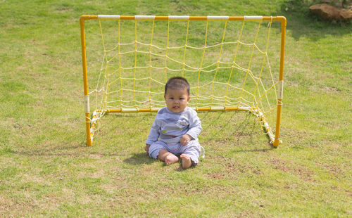 Portrait of cute boy sitting against goal post at soccer field