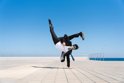 Low angle view of man jumping on beach against clear blue sky