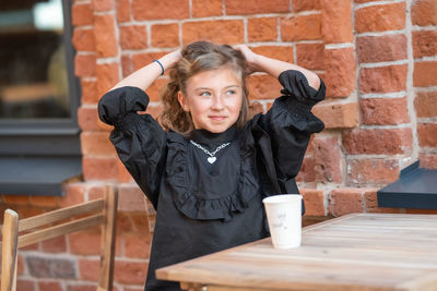 Portrait of smiling woman with coffee cup against brick wall