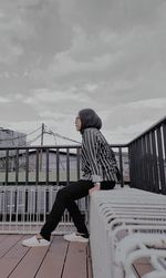 Side view of man standing on footbridge against sky