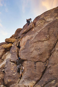 Low angle view of men climbing rock against sky