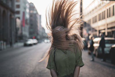 Young woman tossing hair while standing on city street