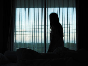 Silhouette woman standing against window at home 