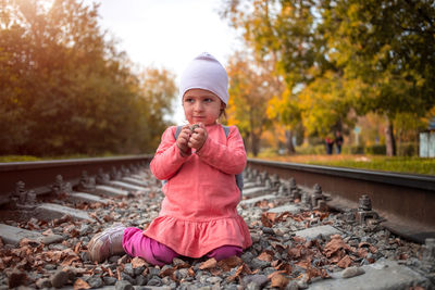 Portrait of young woman drinking water while sitting on retaining wall