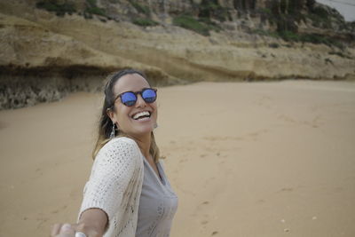 Portrait of smiling young woman wearing sunglasses standing at beach