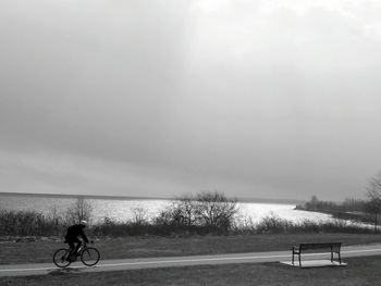 Man riding bicycle on shore against sky