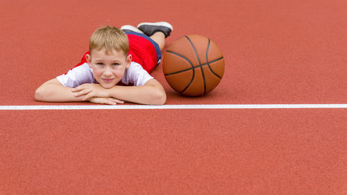 Portrait of boy lying with basketball on sports court
