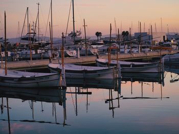 Sailboats moored in harbor at sunset