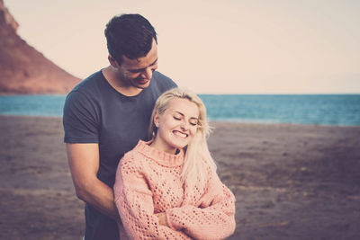 Smiling young couple at beach against clear sky