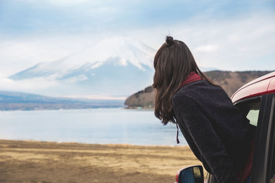 Rear view of woman with umbrella on shore against sky